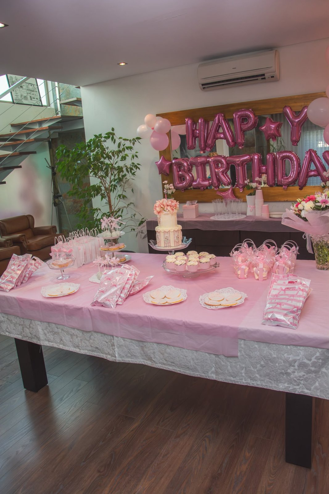 Mesa de festa comprida forrada a rosa, com bolo, doces e lembranças
